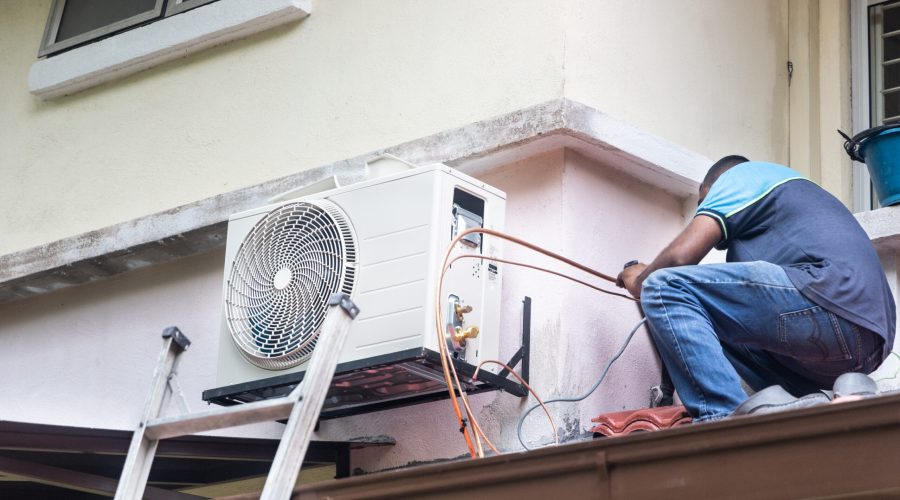 Technician installing outdoor air conditioner compressor unit on outdoor wall